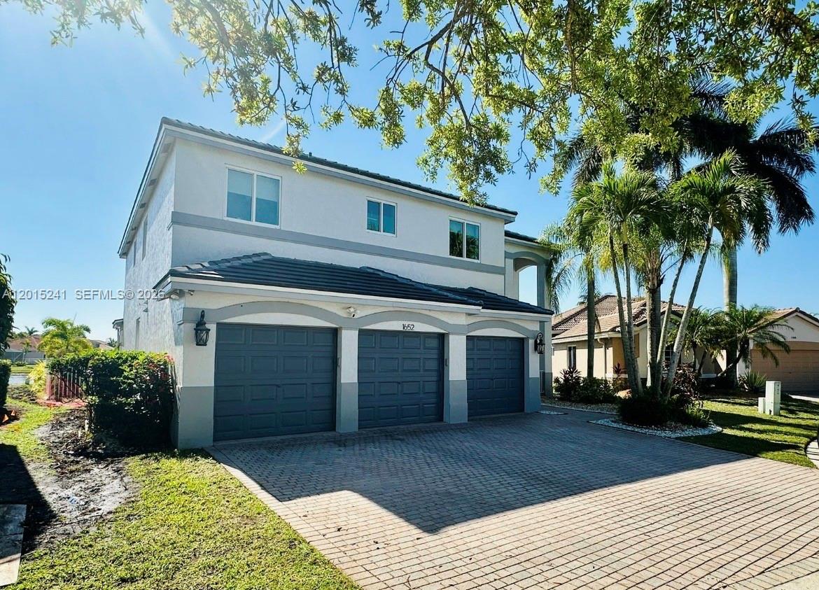 A two-story house features a three-car garage and a paved driveway under a sunny sky — 1652 Orchid Bnd, Weston FL 33327, WESTON, FL