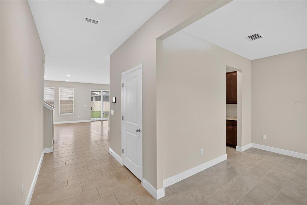 A view of a tiled hallway leading to an open living area with sliding doors — 2546 WARREN ACRES BOULEVARD, WESLEY CHAPEL, FL