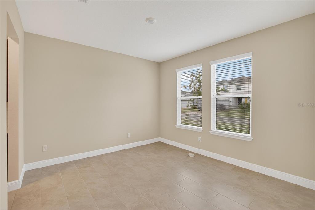 An empty room with beige walls, tile flooring, and two windows overlooking a neighborhood — 2546 WARREN ACRES BOULEVARD, WESLEY CHAPEL, FL