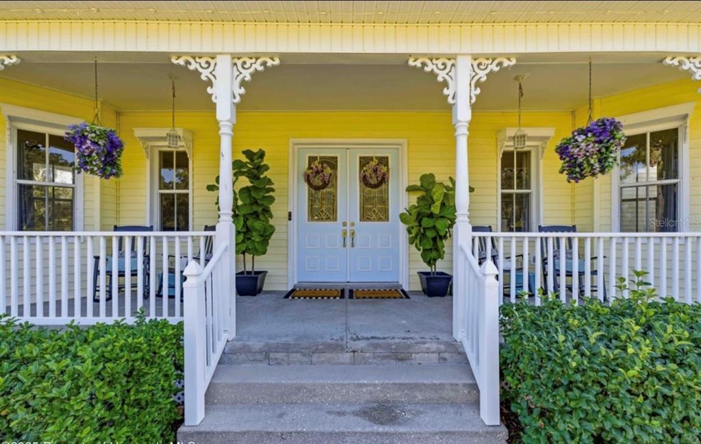 A yellow house features a front porch with white railings, double doors, and hanging plants — 23327 EPPLEY DRIVE, BROOKSVILLE, FL