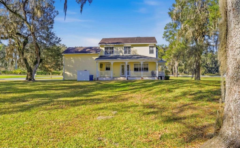 A two-story yellow house with a covered front porch sits on a large grassy lot — 23327 EPPLEY DRIVE, BROOKSVILLE, FL