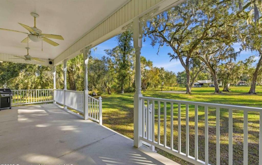 A covered porch with white railings and ceiling fans overlooks a grassy yard with trees — 23327 EPPLEY DRIVE, BROOKSVILLE, FL