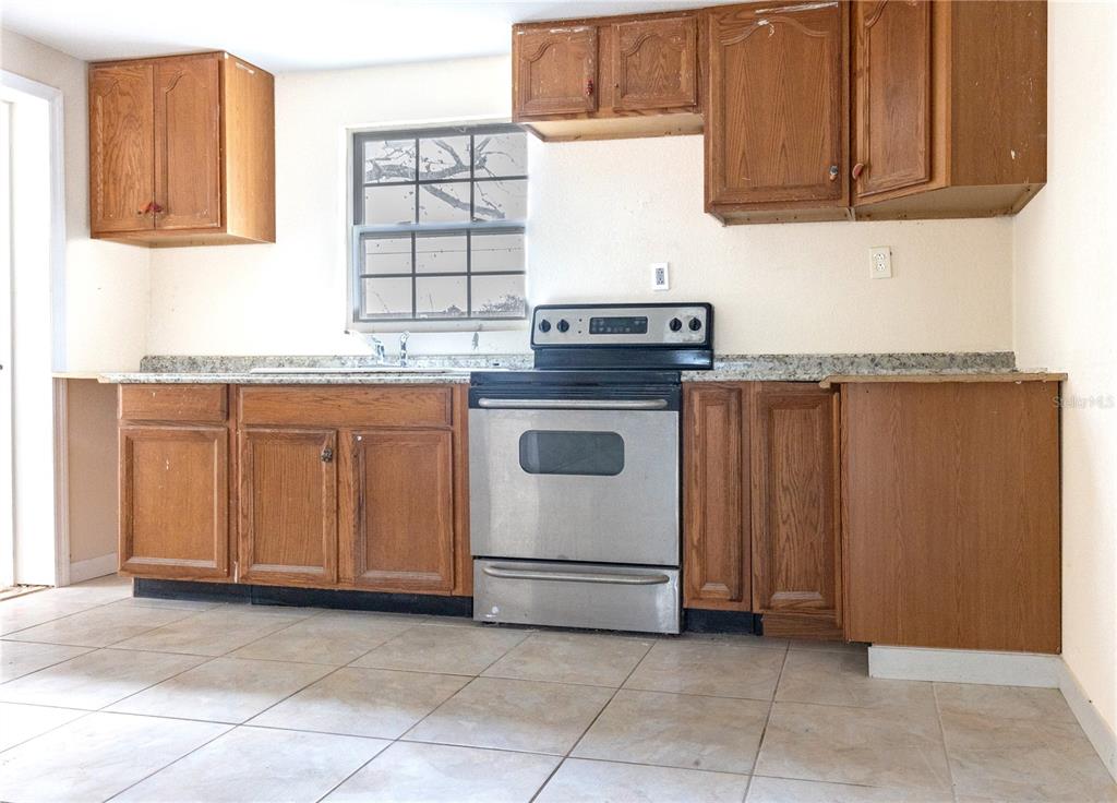 A kitchen features wood cabinets, a stainless steel stove, a window, and tiled flooring — 628 PETERSON STREET, WAUCHULA, FL
