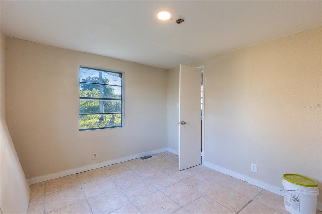 An empty room with beige walls, tiled floors, a single window, and an open door — 628 PETERSON STREET, WAUCHULA, FL
