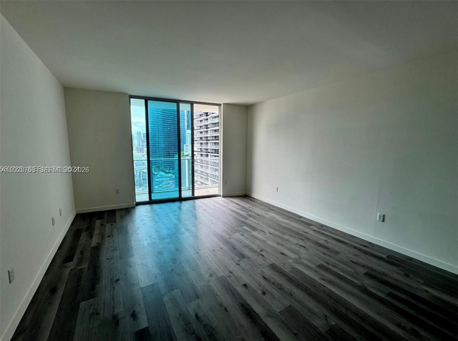 An empty room features dark wood-look flooring, white walls, and a sliding glass balcony door — 1100 S Miami Ave # 2409, Miami FL 33130, MIAMI, FL
