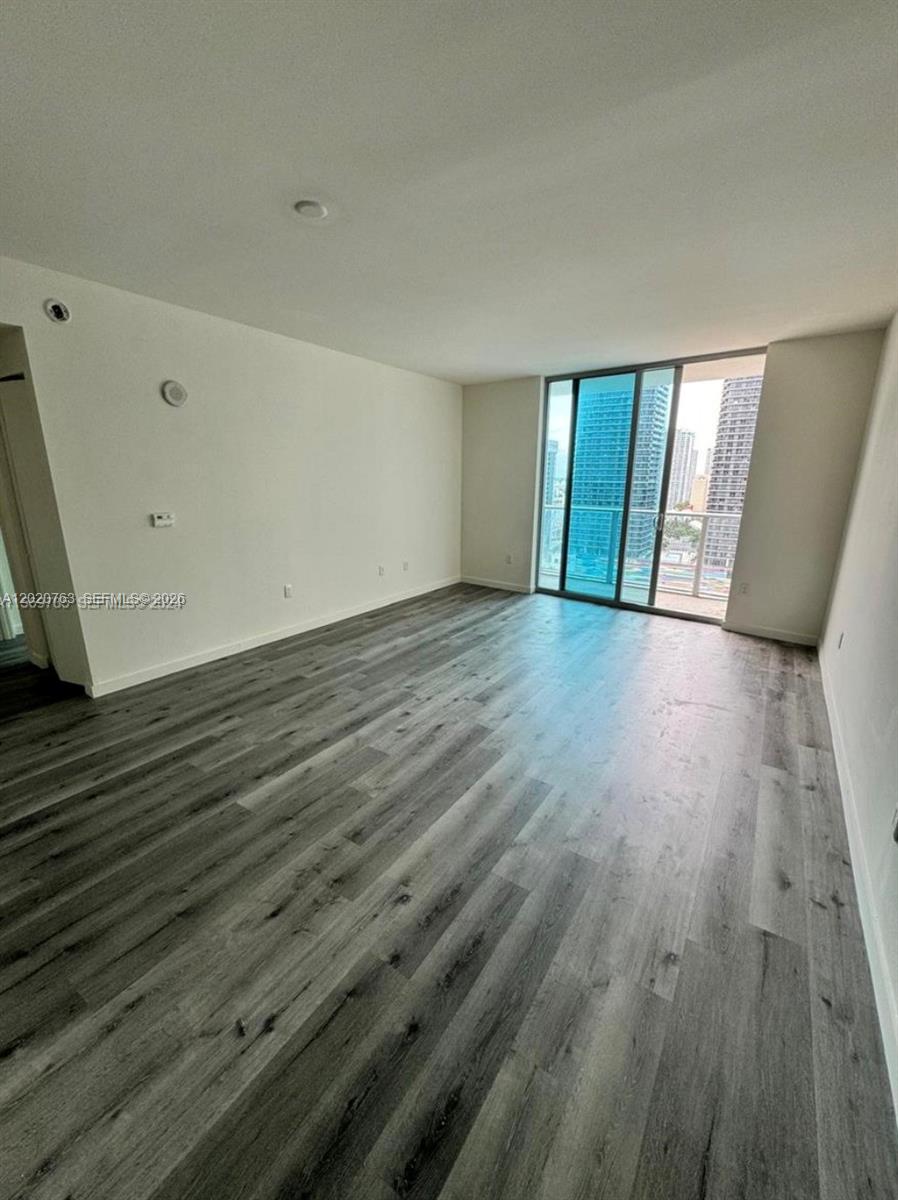 An empty room features light-colored walls, gray wood-look flooring, and a sliding glass balcony door — 1100 S Miami Ave # 2409, Miami FL 33130, MIAMI, FL