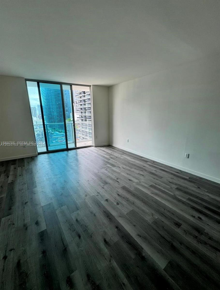 An empty room with gray wood-look flooring and a sliding glass door leading to a balcony — 1100 S Miami Ave # 2409, Miami FL 33130, MIAMI, FL