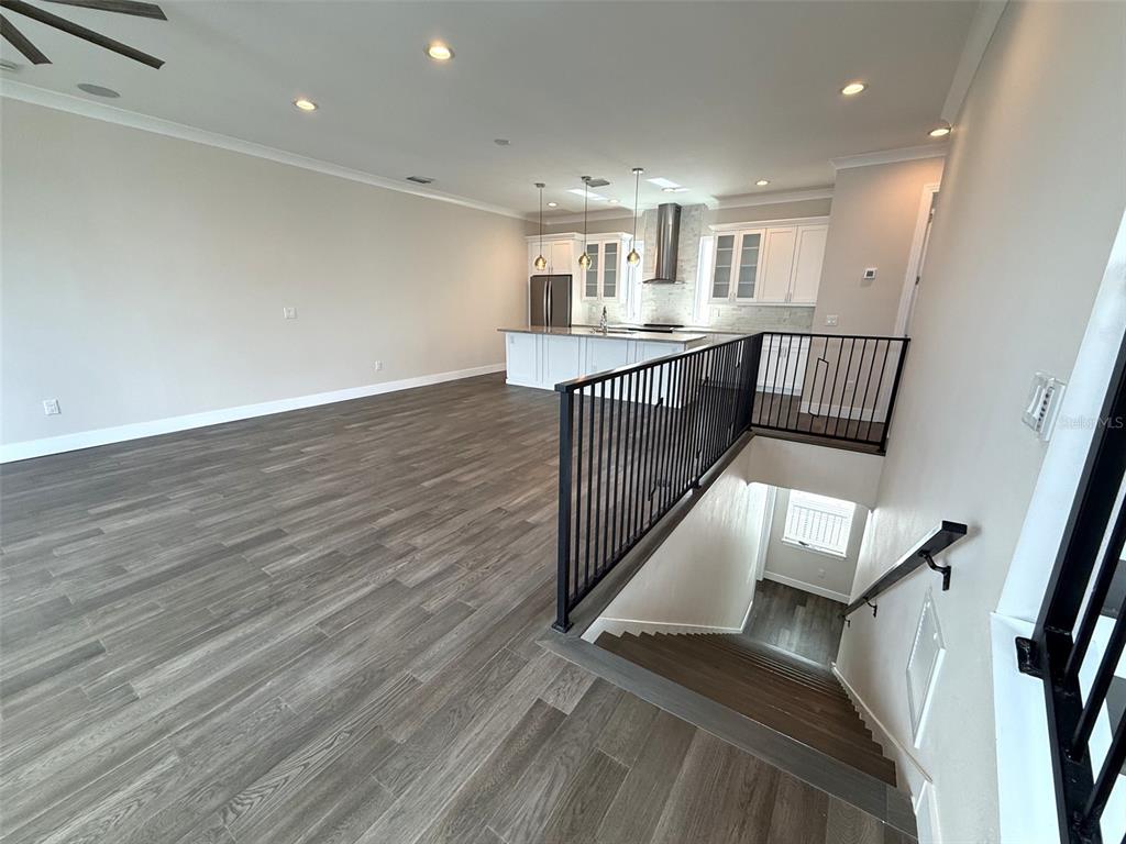 An open-concept kitchen and living area features wood-look flooring and a staircase with railings — 4910 W MCELROY AVENUE UNIT 3, TAMPA, FL