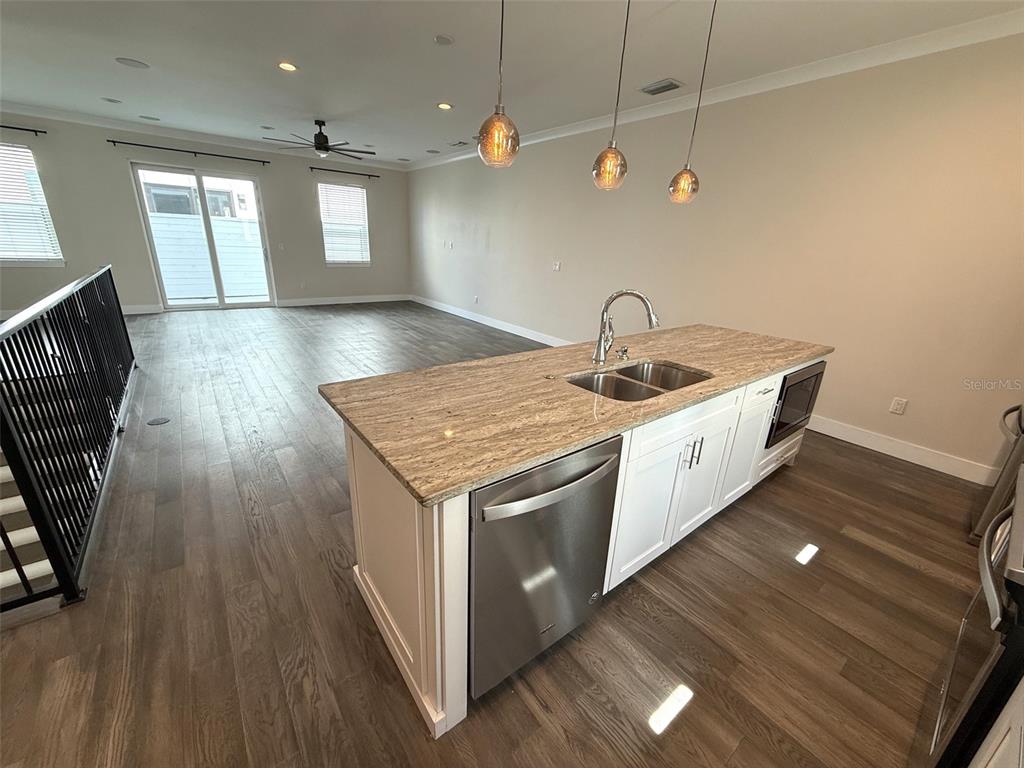 A kitchen island with a stainless steel dishwasher and sink sits before an open living area — 4910 W MCELROY AVENUE UNIT 3, TAMPA, FL