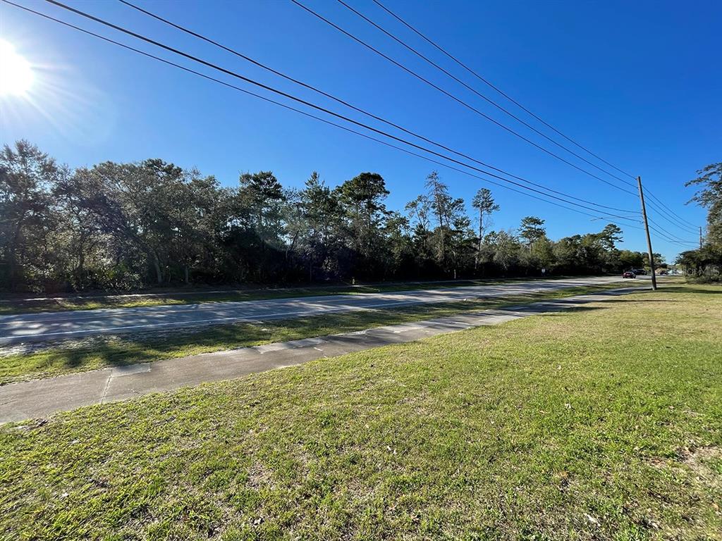 A grassy lot with a sidewalk borders a road lined with trees under a blue sky — 3124 LAKE HELEN OSTEEN ROAD, DELTONA, FL