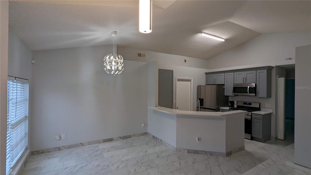 A kitchen with gray cabinets and stainless steel appliances overlooks a dining area with tile — 3048 PINEDA DRIVE, ORLANDO, FL