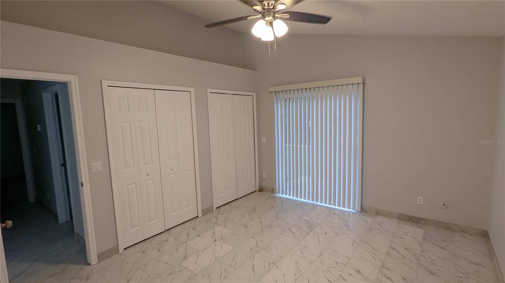 A bedroom with white marble-look tile flooring, two white closets, and vertical blinds on sliding doors — 3048 PINEDA DRIVE, ORLANDO, FL