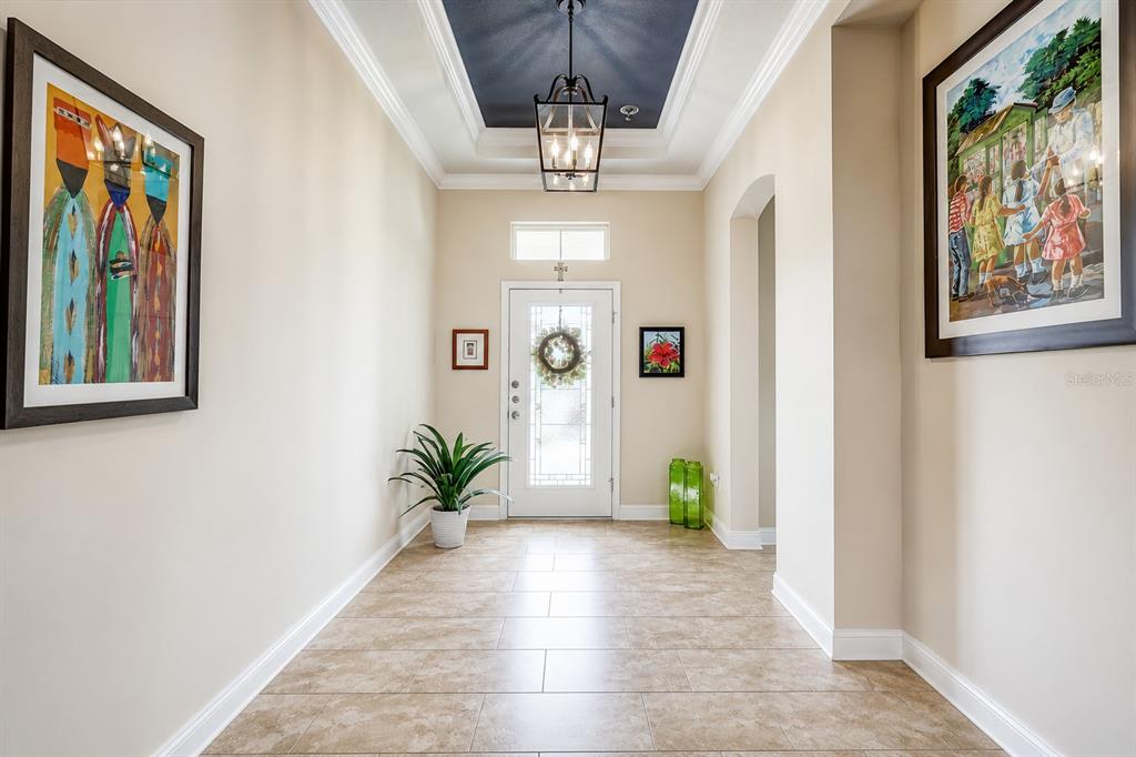 A bright entryway features tile flooring, a tray ceiling with a pendant light, and artwork — 7209 MEETING HOUSE LANE, APOLLO BEACH, FL