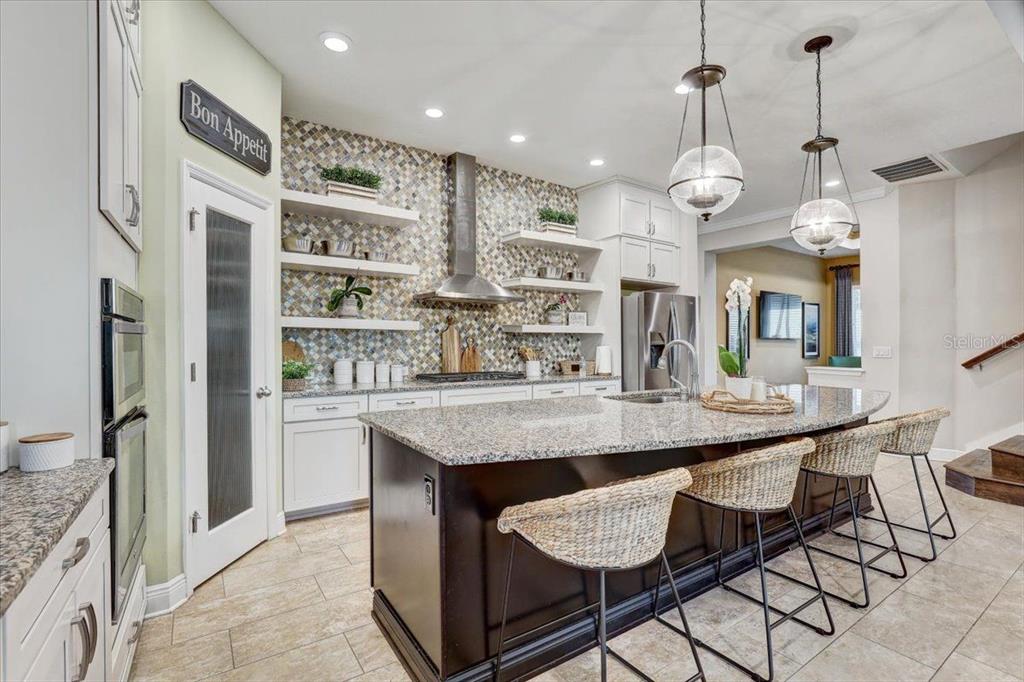 A kitchen features white cabinets, a dark island with wicker stools, and a mosaic backsplash — 7209 MEETING HOUSE LANE, APOLLO BEACH, FL