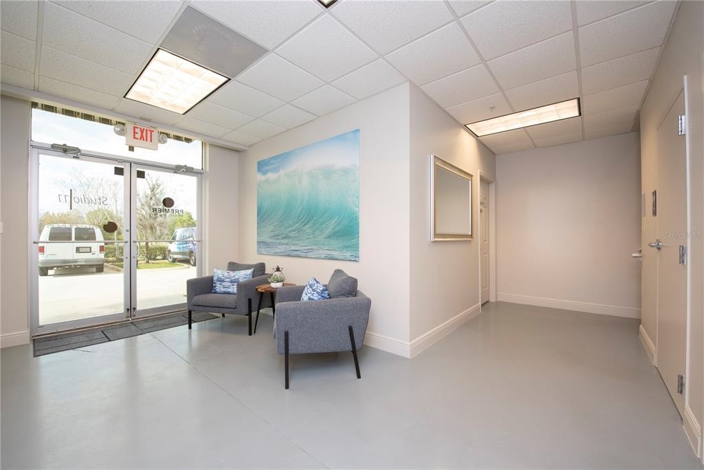 A waiting area features two gray armchairs, a wave wall art, and glass entry doors — 6557 HAZELTINE NATIONAL DRIVE UNIT C, ORLANDO, FL