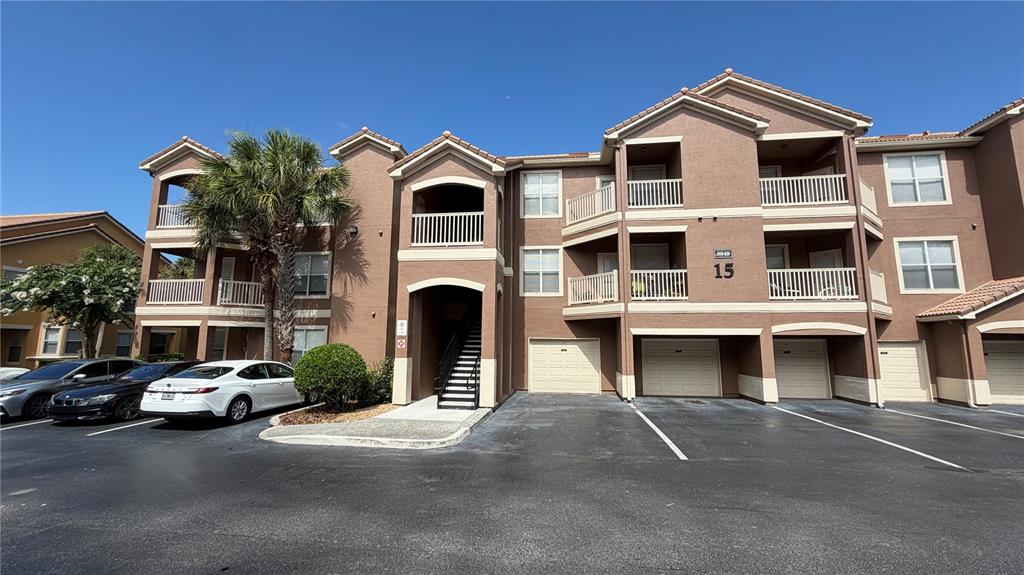 A three-story apartment building features brown stucco walls, balconies, and ground-level garage doors — 8849 VILLA VIEW CIRCLE UNIT 302, ORLANDO, FL