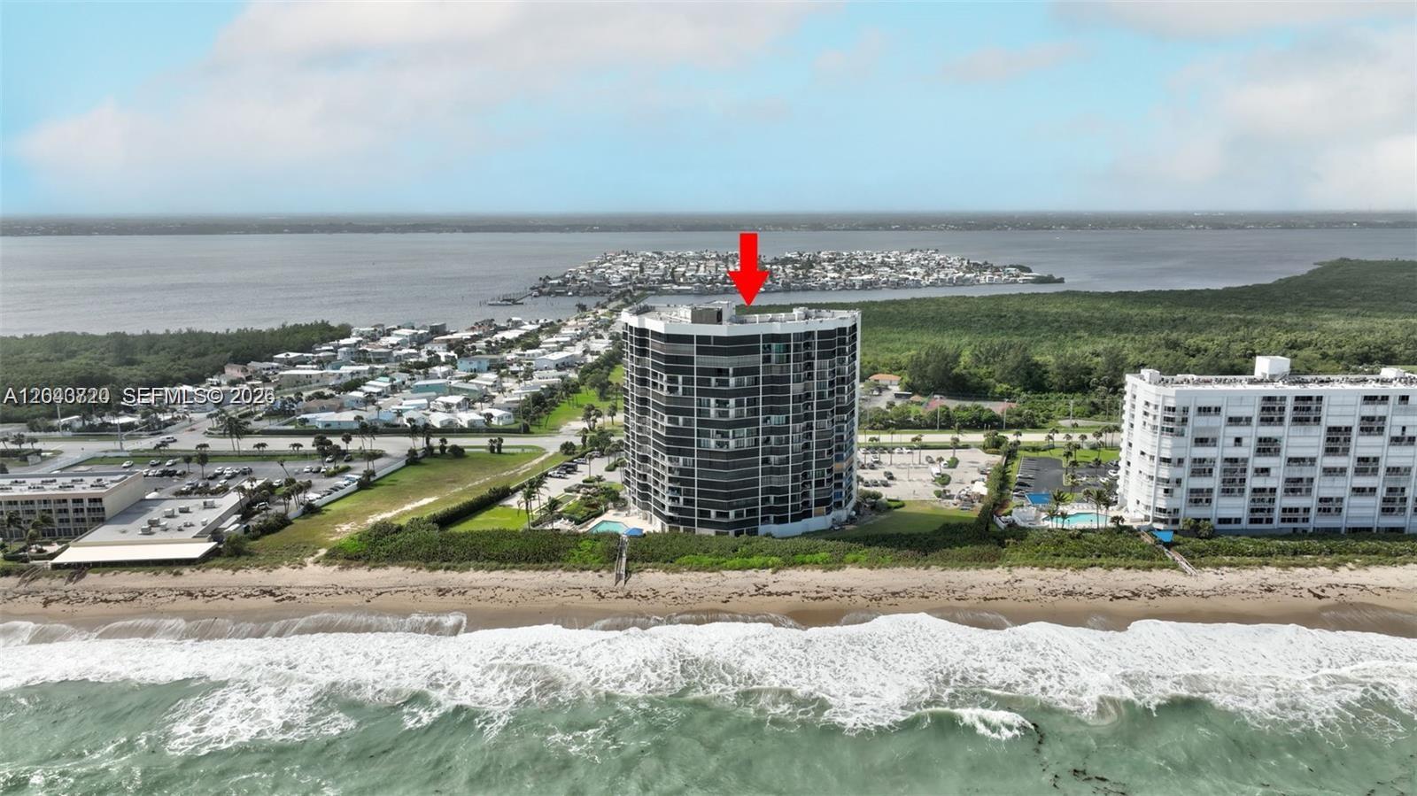 An aerial view shows a tall, dark-colored residential building situated directly on a sandy beach — 9650 S Ocean Dr # 1403, Jensen Beach FL 34957, JENSEN BEACH, FL