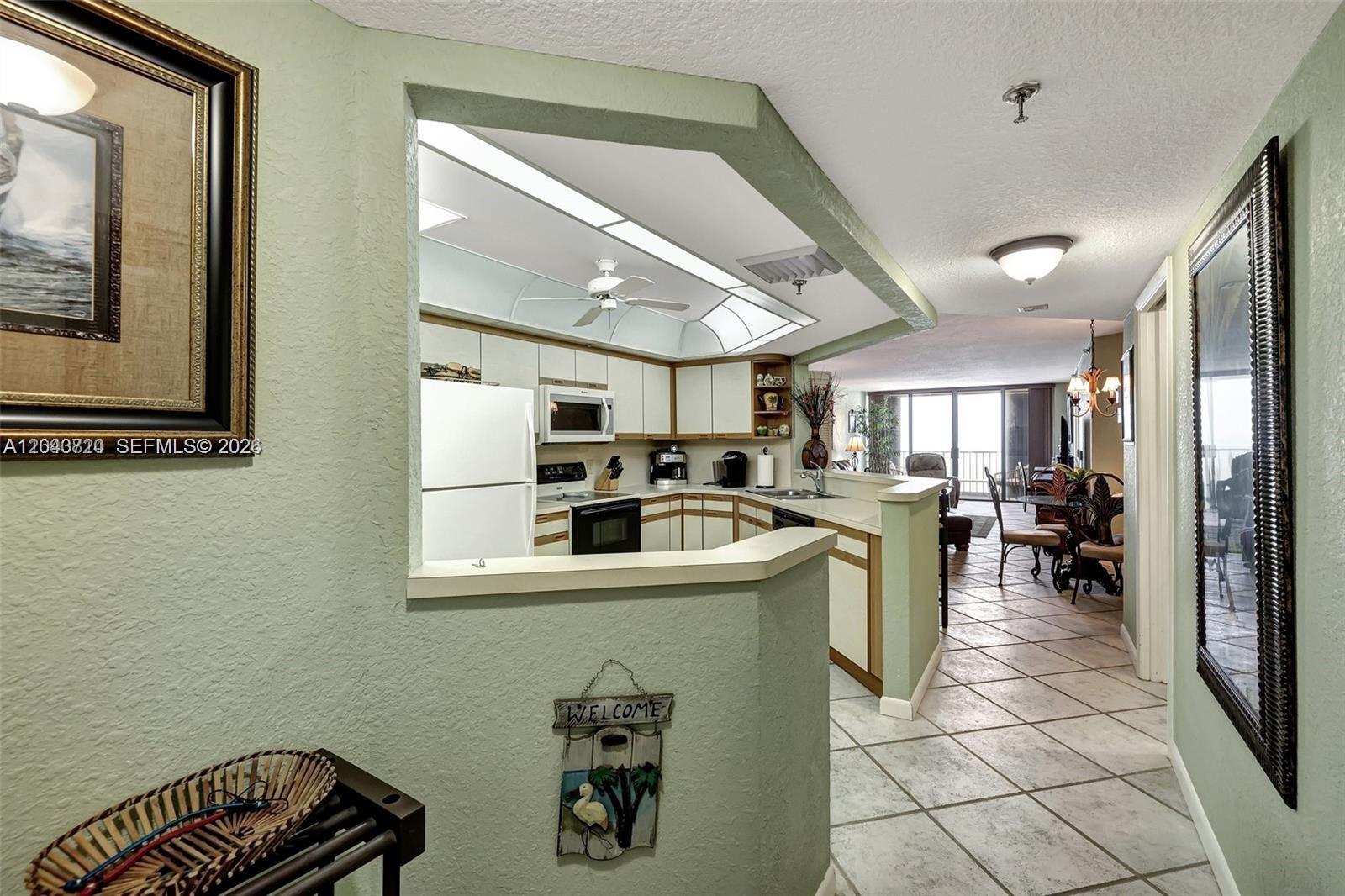 A kitchen with white cabinets and appliances overlooks a dining area and living room — 9650 S Ocean Dr # 1403, Jensen Beach FL 34957, JENSEN BEACH, FL