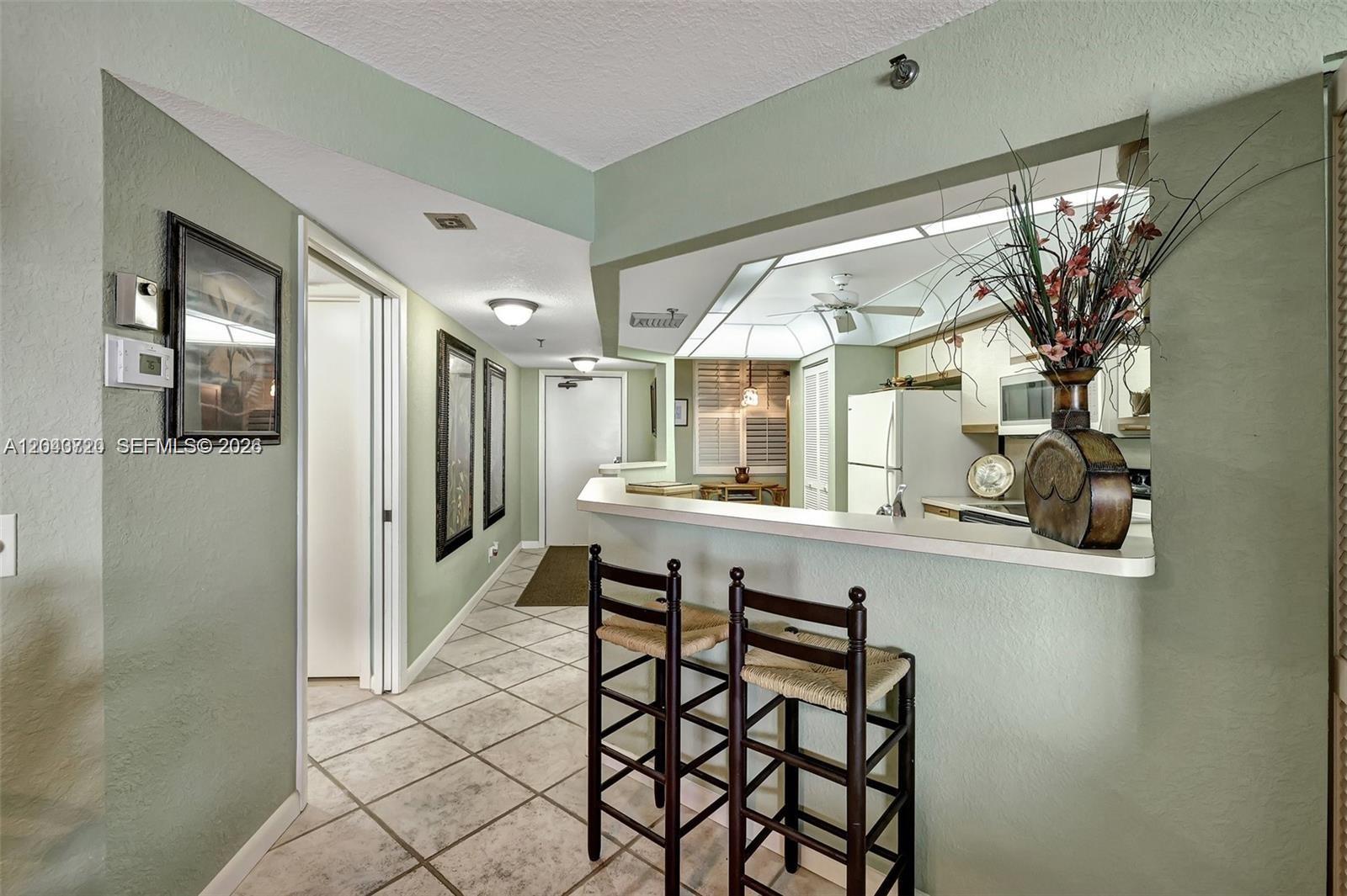 A kitchen pass-through window overlooks a hallway with tile flooring and two bar stools — 9650 S Ocean Dr # 1403, Jensen Beach FL 34957, JENSEN BEACH, FL
