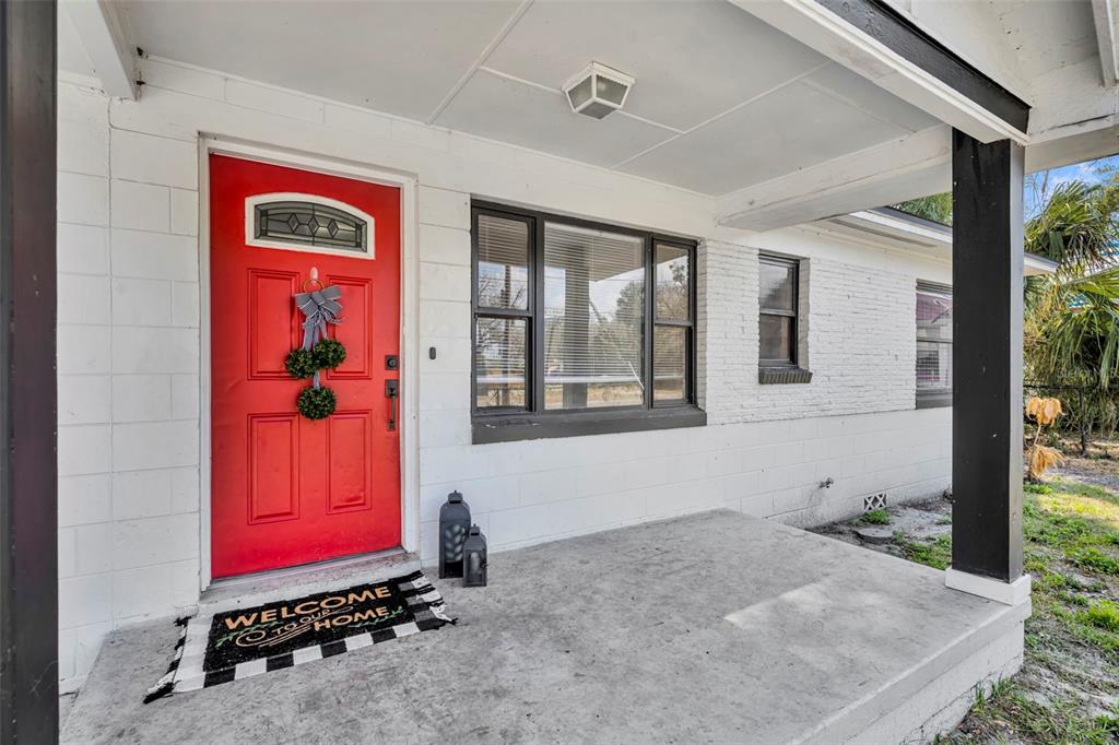 A white brick house exterior features a bright red front door and a concrete porch — 1307 SHEPHERD AVENUE, SANFORD, FL