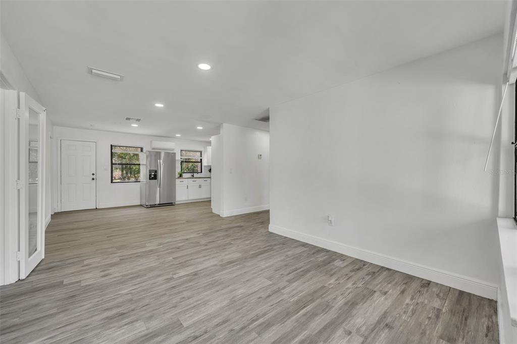 An open-concept living area with light wood-look flooring, white walls, and a kitchen in back — 1307 SHEPHERD AVENUE, SANFORD, FL