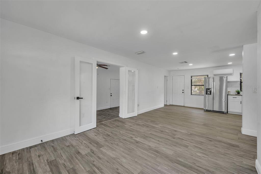 A bright, open-concept living area with white walls, wood-look flooring, and French doors — 1307 SHEPHERD AVENUE, SANFORD, FL