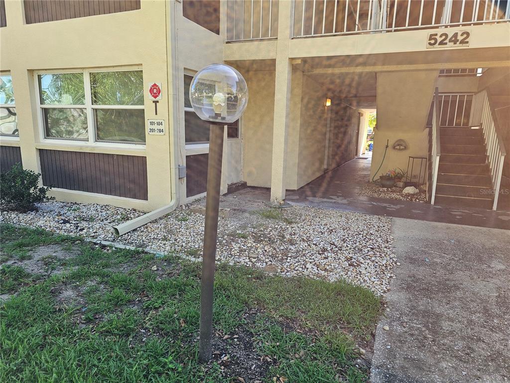 An exterior view of an apartment building entrance with a globe light and stairs — 5242 OPAL LANE UNIT 101, NEW PORT RICHEY, FL