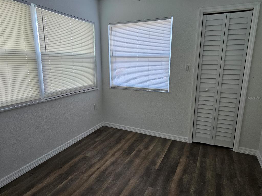 A room with wood-look flooring, white walls, two windows with blinds, and a louvered closet door — 5242 OPAL LANE UNIT 101, NEW PORT RICHEY, FL