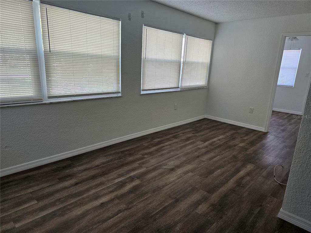 An empty room features wood-look flooring, white walls, and two sets of windows with blinds — 5242 OPAL LANE UNIT 101, NEW PORT RICHEY, FL