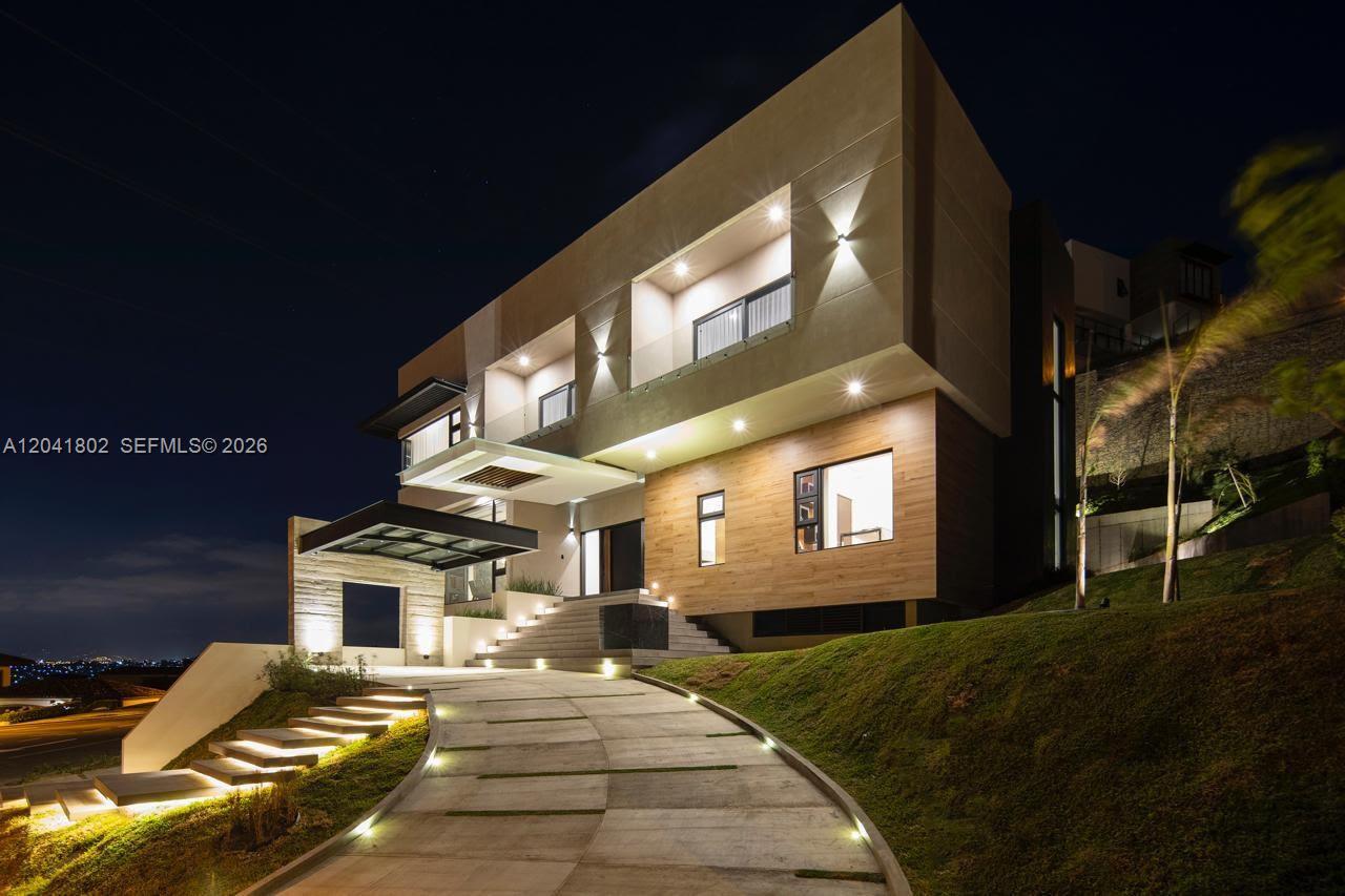 A modern multi-story house at night with a curved driveway and illuminated exterior features — 37-3 ESCAZU, CR 1556-M-000, CR