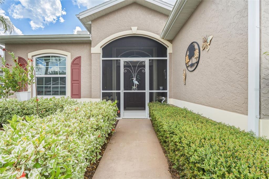 A concrete walkway leads to the front entrance of a house with a screened door — 1351 HEDGEWOOD CIRCLE, NORTH PORT, FL