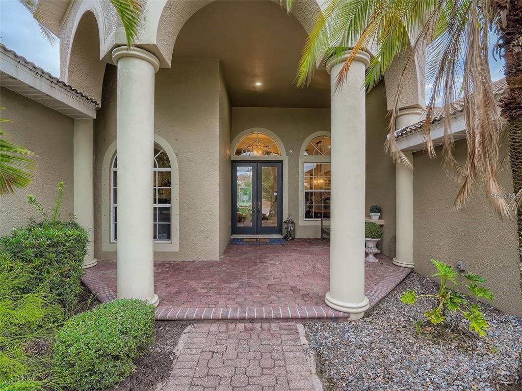 A covered entryway features two large columns, a brick paver walkway, and double glass doors — 7742 CAMDEN HARBOUR DRIVE, BRADENTON, FL