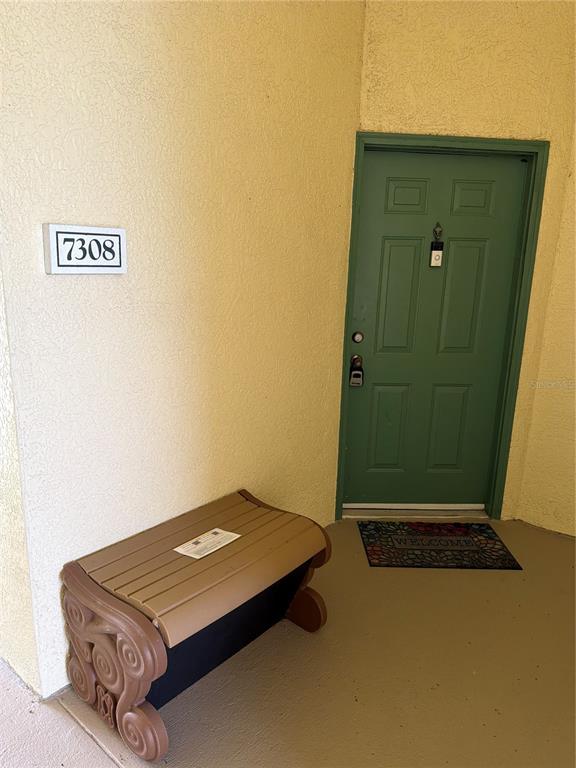 A green front door with a welcome mat and a storage bench sits outside — 8815 DUNES COURT UNIT 308, KISSIMMEE, FL