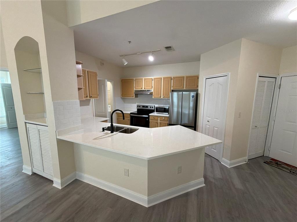 A kitchen features light wood cabinets, white countertops, stainless steel appliances, and a breakfast bar — 8815 DUNES COURT UNIT 308, KISSIMMEE, FL