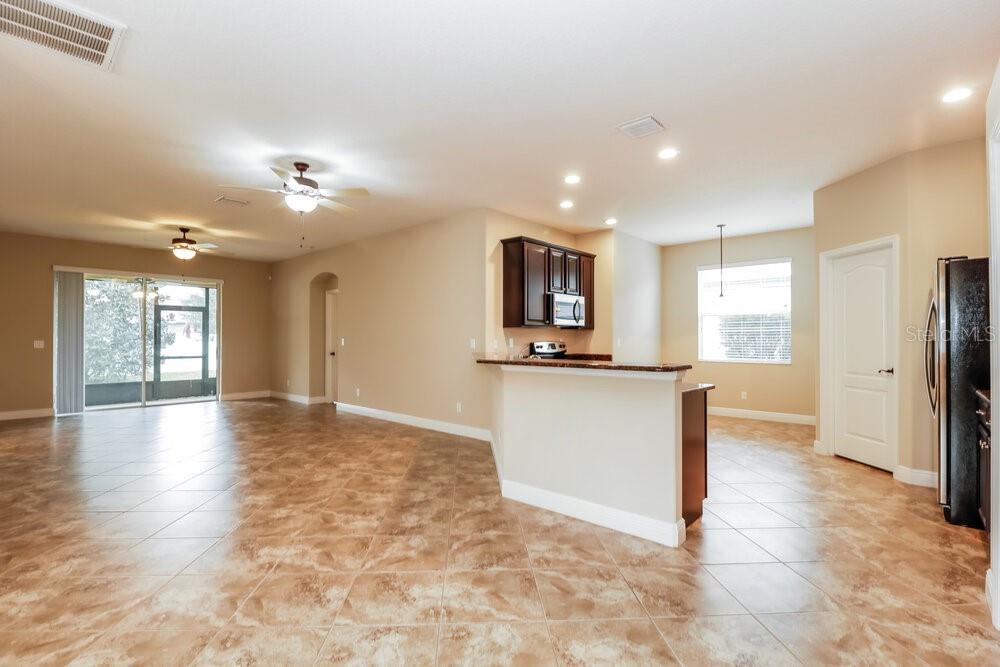 An open-concept kitchen and living area feature tile flooring, dark wood cabinets, and sliding doors — 12307 CRICKLEWOOD DRIVE, SPRING HILL, FL