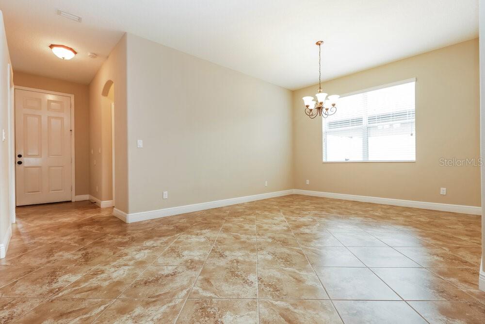 An empty dining room features tan tile flooring, beige walls, and a hanging light fixture — 12307 CRICKLEWOOD DRIVE, SPRING HILL, FL