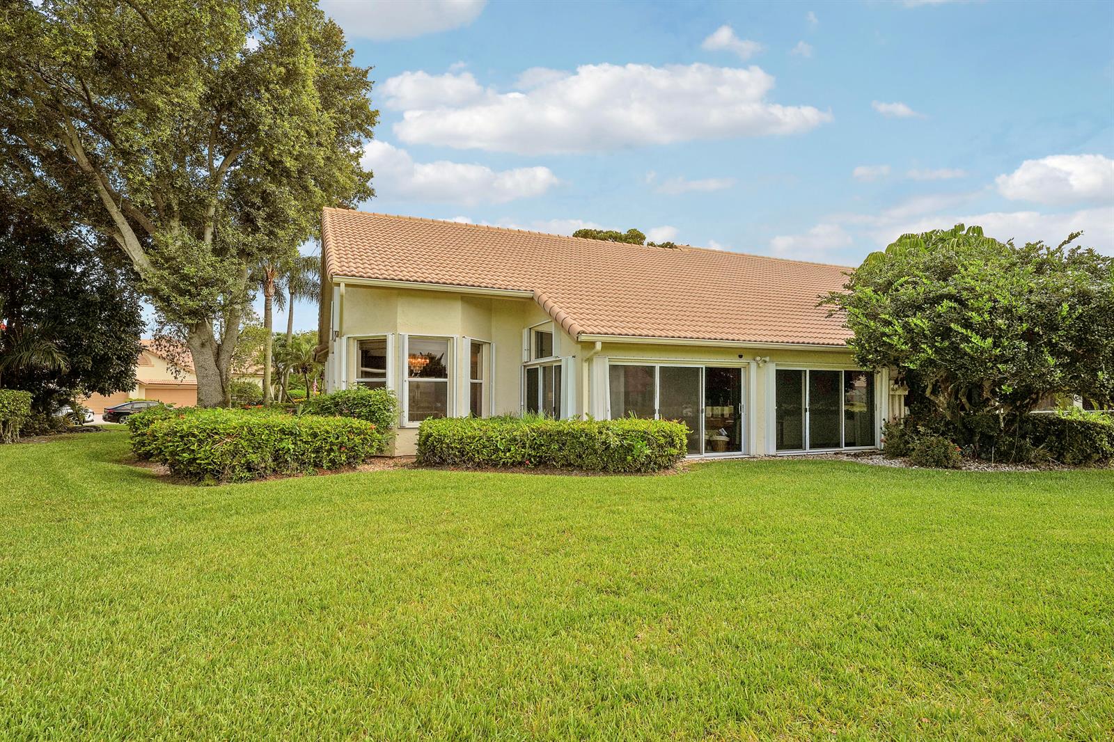 The exterior of a single-story house with a tiled roof, sliding glass doors, and landscaping — 7136 Ashford Lane, Boynton Beach FL 33472, BOYNTON BEACH, FL