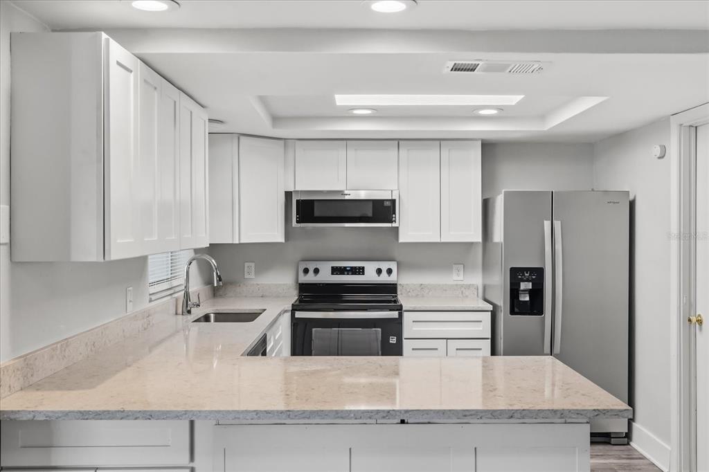 A kitchen with white cabinets, stainless steel appliances, and light-colored stone countertops — 3435 GULF COAST DRIVE, HERNANDO BEACH, FL