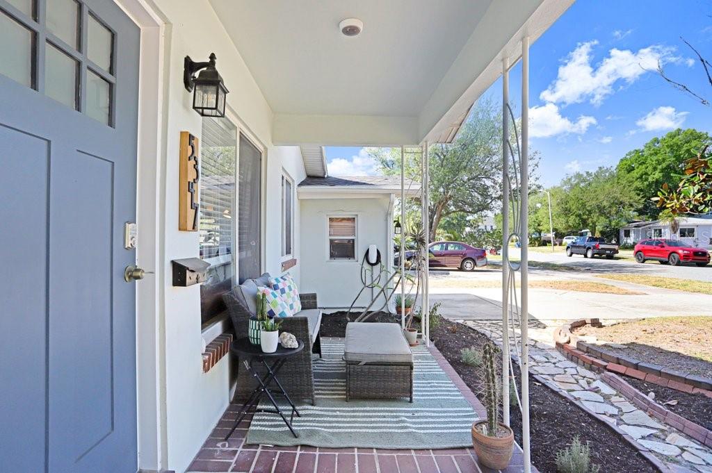 A covered front porch features a blue door, patio furniture, and a brick floor — 5347 10TH STREET N, ST PETERSBURG, FL