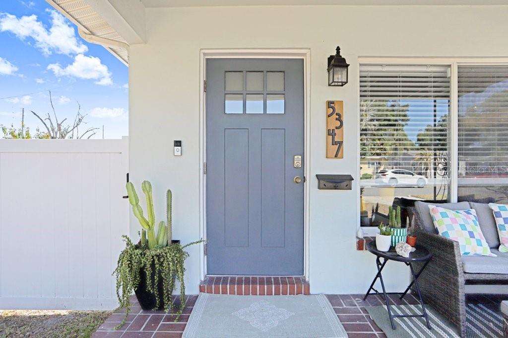 A blue front door with a window sits on a brick porch next to a window — 5347 10TH STREET N, ST PETERSBURG, FL