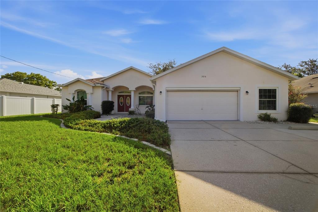 A single-story house with a white stucco exterior, a two-car garage, and a front lawn — 3016 MANDRELL AVENUE, SPRING HILL, FL