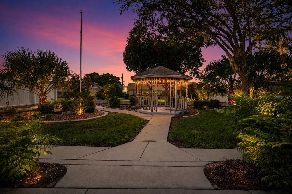 A wooden gazebo sits at the end of a concrete walkway in a landscaped yard — 3016 MANDRELL AVENUE, SPRING HILL, FL