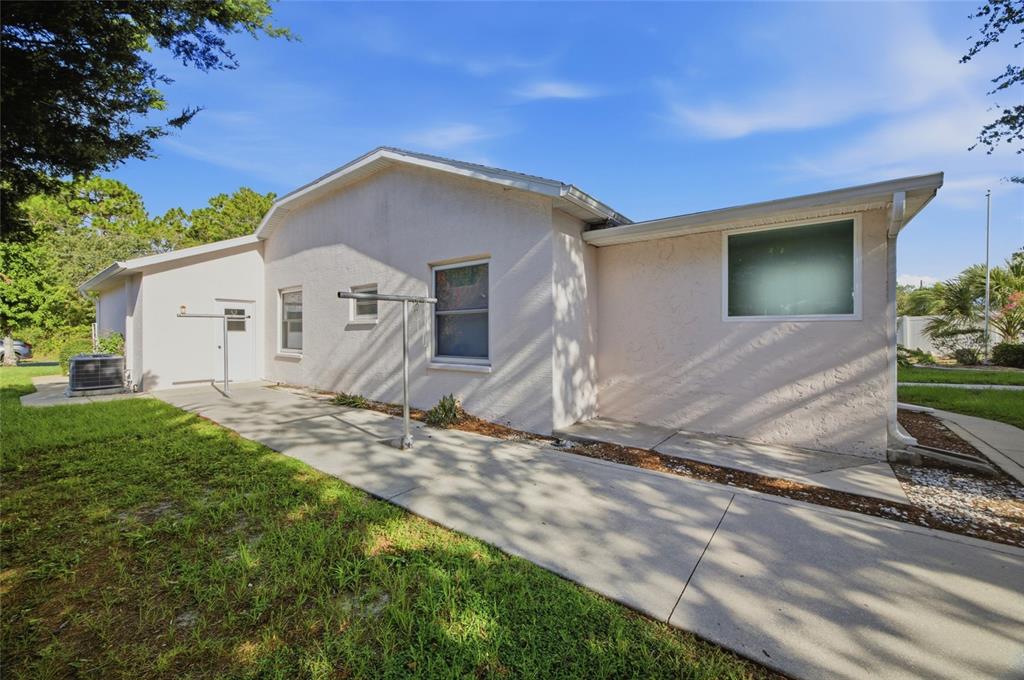 The exterior of a light-colored house features a concrete patio, a clothesline, and a window — 3016 MANDRELL AVENUE, SPRING HILL, FL