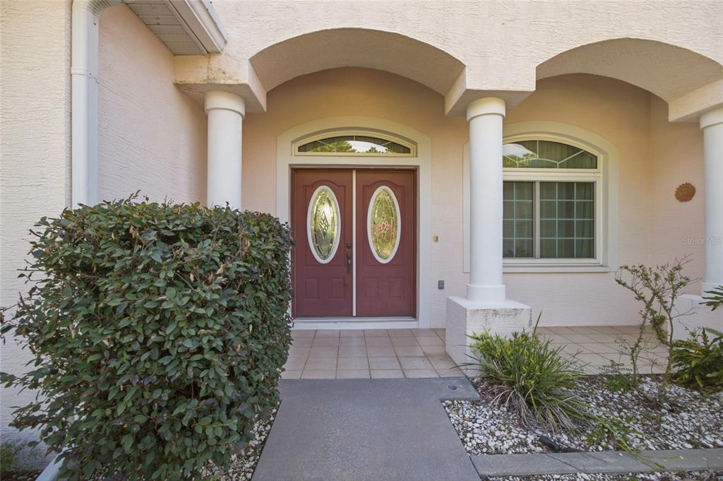 A front entrance with double red doors, arched architectural details, and two white columns — 3016 MANDRELL AVENUE, SPRING HILL, FL