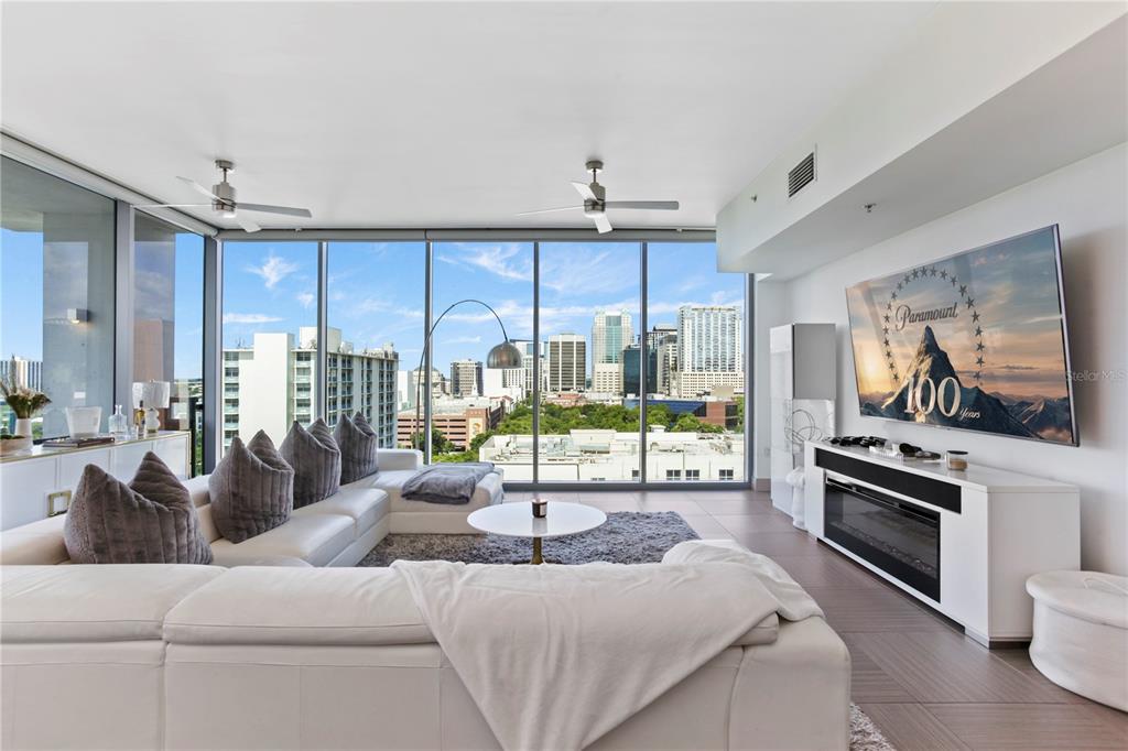 A modern living room features a white sectional sofa, fireplace console, and floor-to-ceiling city views — 260 S OSCEOLA AVENUE UNIT 1106, ORLANDO, FL