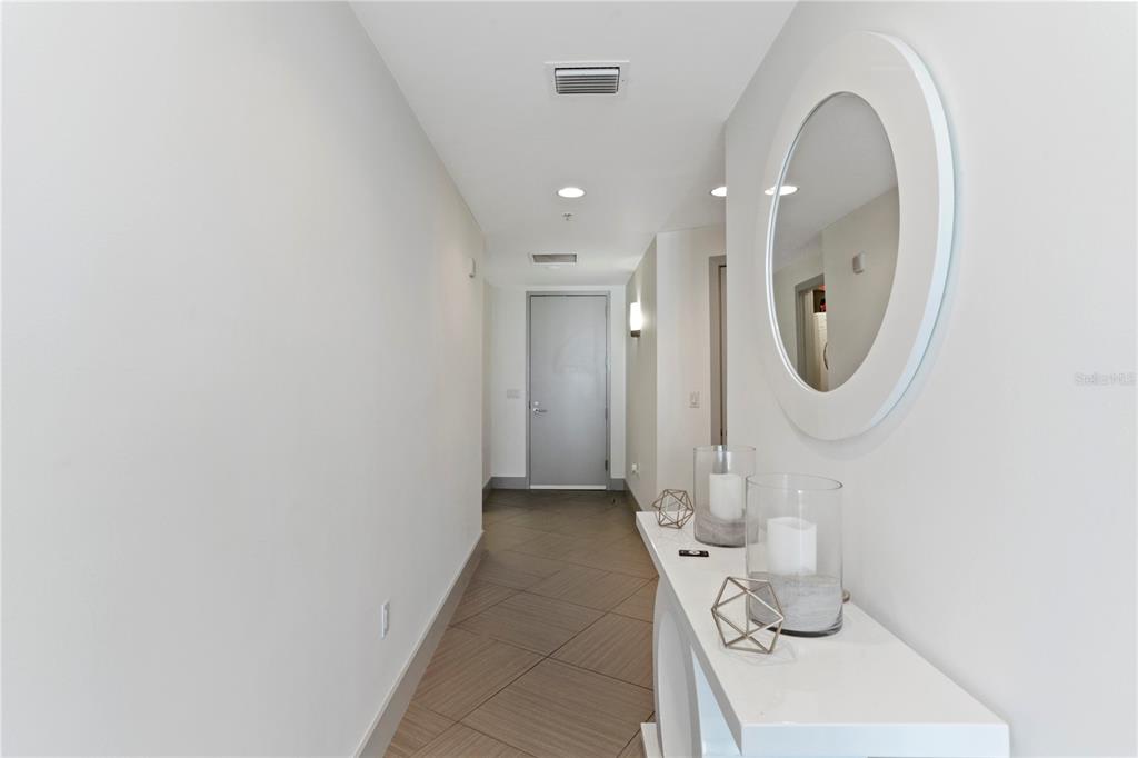 A hallway features light-colored walls, tile flooring, a white console table, and a round mirror — 260 S OSCEOLA AVENUE UNIT 1106, ORLANDO, FL