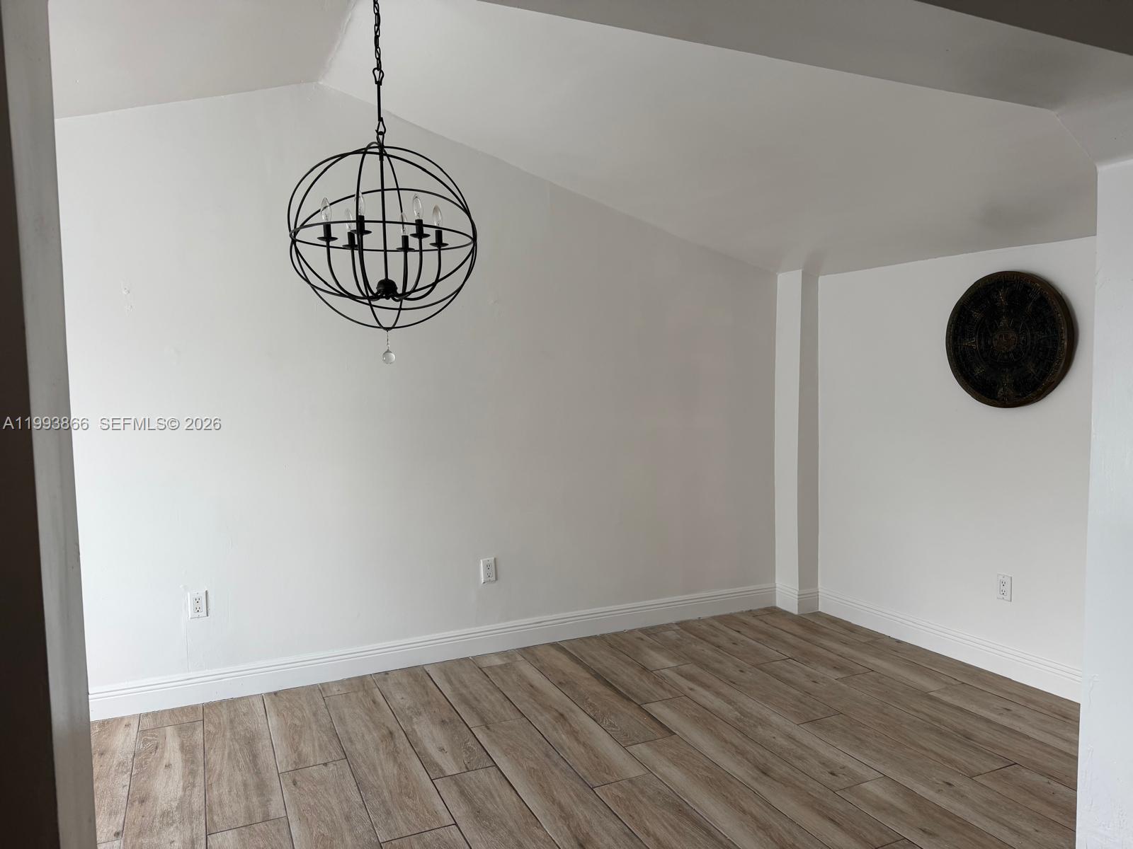 An empty room features white walls, wood-look tile flooring, and a black orb chandelier — 3427 SW 64th Ave, Miami FL 33155, MIAMI, FL