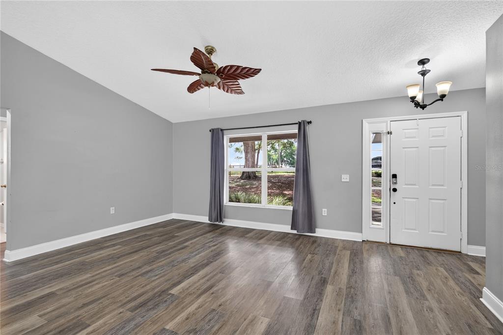 An empty living room features gray walls, wood-look flooring, a ceiling fan, and a front door — 24307 ADAIR AVENUE, SORRENTO, FL