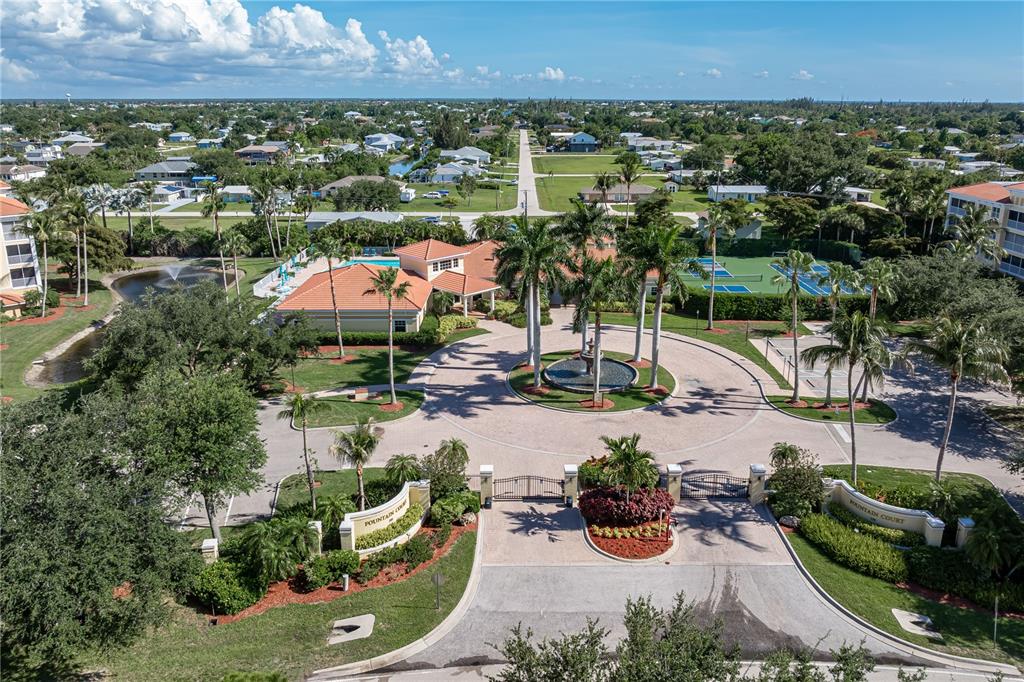 An aerial view shows the gated entrance, circular driveway, fountain, and clubhouse of a residential community — 255 WEST END DRIVE UNIT 4205, PUNTA GORDA, FL