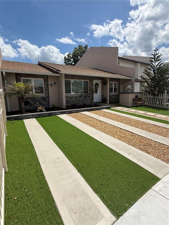 A single-story house features a stone facade, artificial turf driveway, and a white picket fence — 2710 CHARING CROSS WAY, ORLANDO, FL